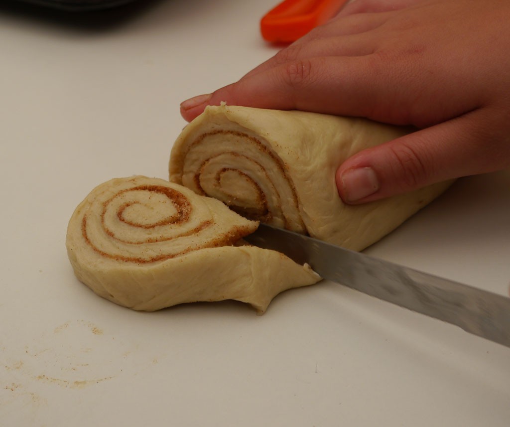 Hand von einem Kind, das eine Scheibe von einer Teigrolle abschneidet.
