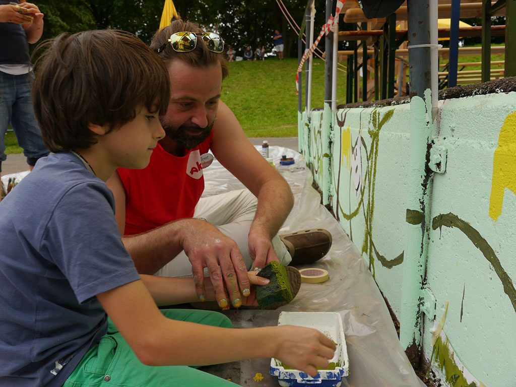 Ein Künstler erklärt einem Kind, wie man eine Wandgestaltung vornimmt.