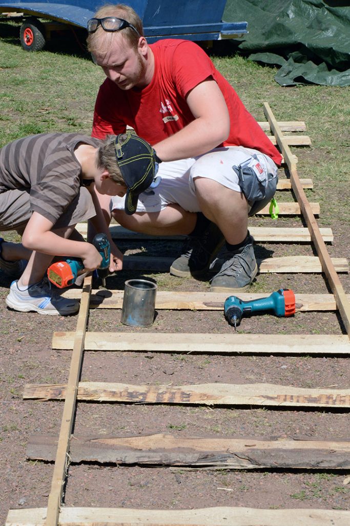 Ein Betreuer unterstützt ein Kind beim Zusammenschrauben von Schienen im Park.