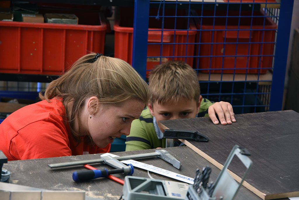 Betreuerin hilft einem Jungen beim Einspannen eines Werkstücks