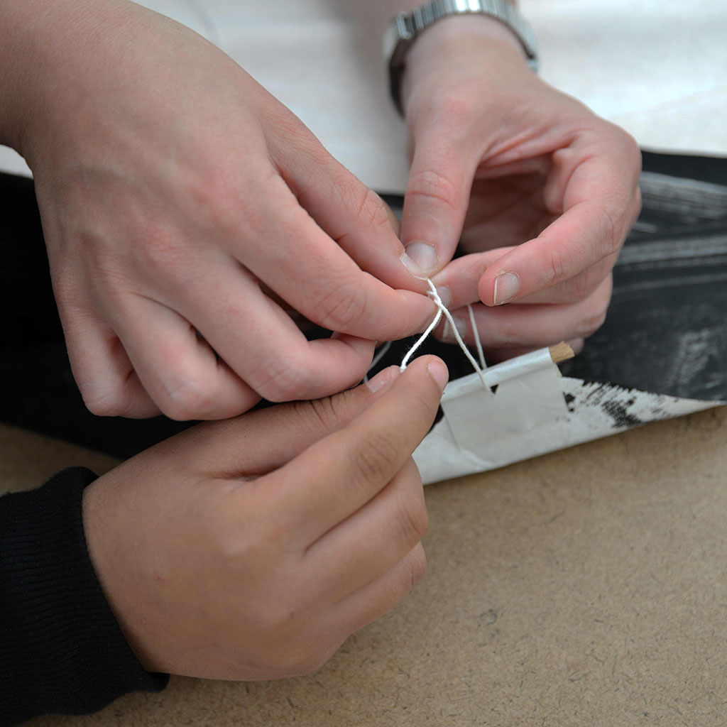 Die Hände eines Erwachsenes helfen einer Kinderhand beim Knoten einer Drachenschnur.
