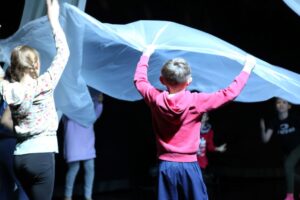 Kinder werfen großes Tuch hoch.