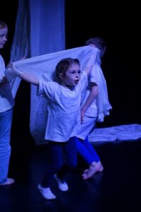 Mädchen mit weißem Tuch in Aktion auf dunkler Bühne.